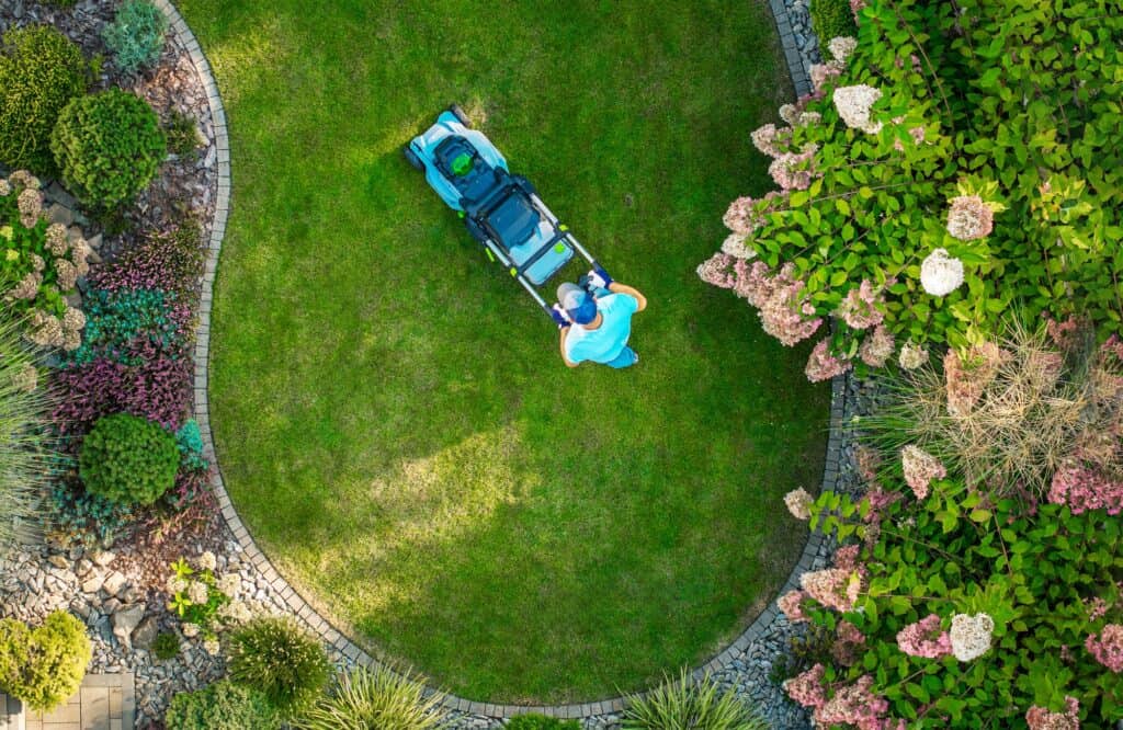 A Person Mowing a Circular Lawn Surrounded by Colorful Flowers in a Landscaped Garden